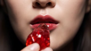 a young woman with glossy red lips biting a glass-like strawberry